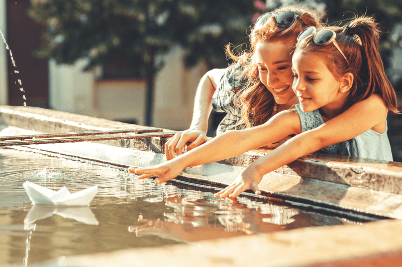 Mother and daughter playing with paper boats in the fountain in they garden.